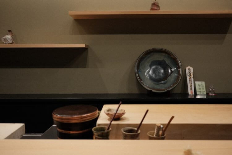 Sushi counter with small bowls and wooden shelves.