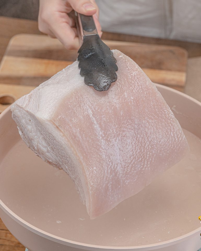 หมูกรอบหม้อทอด ขั้นที่ 3: ใช้ที่คีบยกหมูขึ้นจากน้ำ วางบนเขียงพักไว้จนพอจับได้
