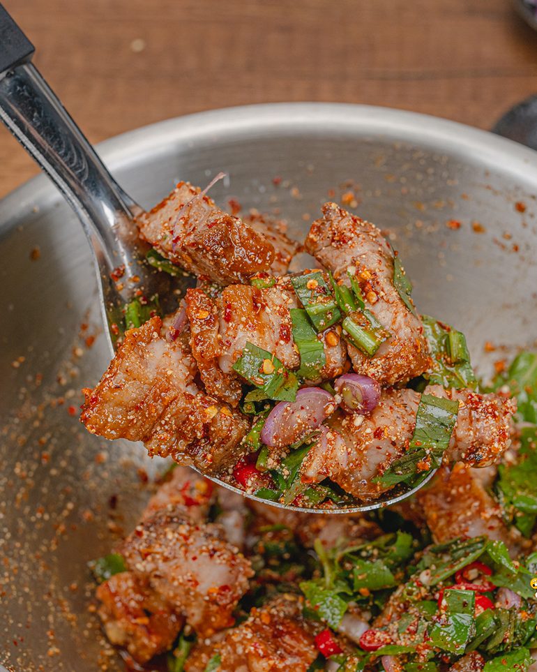 ลาบหมูกรอบ ขั้นที่ 8: ใช้ทัพพีตักพลิกจากก้นชามเบาๆ 4–5 ครั้ง พอให้น้ำลาบกับข้าวคั่วเกาะหมูทั่ว…