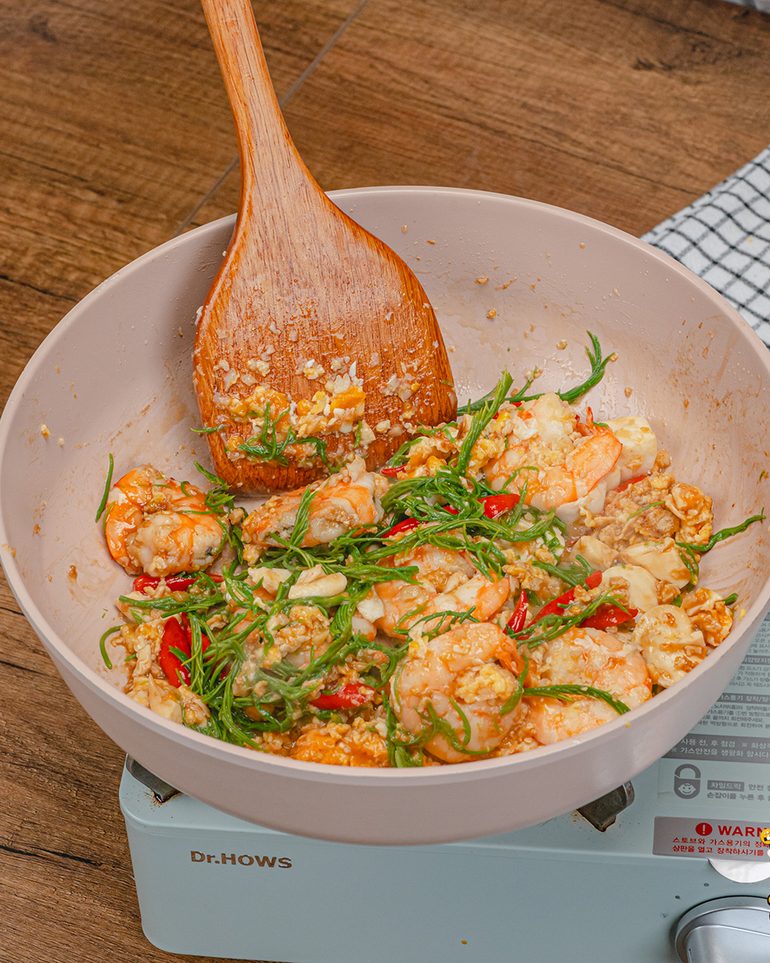 ผัดชะอมกุ้งไข่เค็ม ขั้นที่ 7: ใส่ชะอมลงไป ผัดเร็วๆ ราว 30 วินาที–1 นาที พอใบเริ่มสลดก็ปิดไฟ ตักขึ้นจานทันที